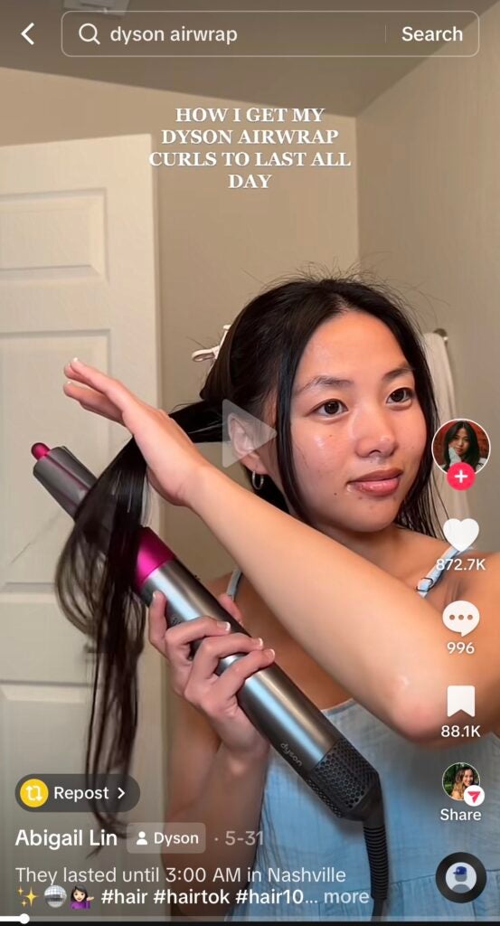 A screenshot of an example of influencer marketing on TikTok. The image shows a TikTok video where an influencer is demonstrating curling her hair with a Dyson Air Wrap.